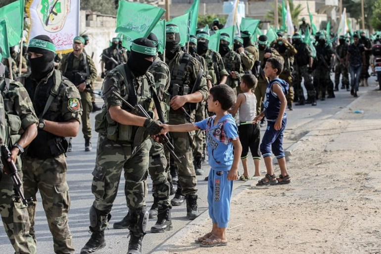 أطفال فلسطينيون يحيون مقاتلي كتائب عز الدين القسام، الجناح المسلح لحركة حماس الفلسطينية، يسيرون في شوارع مدينة خان يونس في جنوب قطاع غزة في 20 يوليو 2017. (Photo: SAID KHATIB / AFP) )